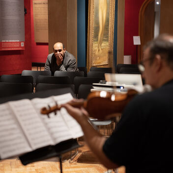 A photograph of composer, Des Oliver looking at a man playing the violin whilst reading sheet music