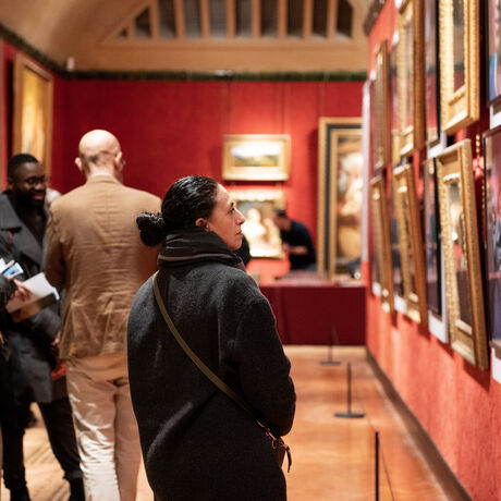 A photograph of the inside of the Historic Galleries during the opening of an exhibition, people stand and look at the art work on the walls