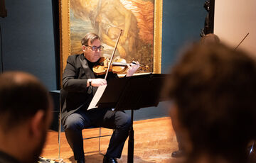 A photograph of a man playing the violin reading sheet music in the Historic Galleries
