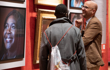 A photograph of two men smiling looking at portraits hung on the wall in the Historic Galleries