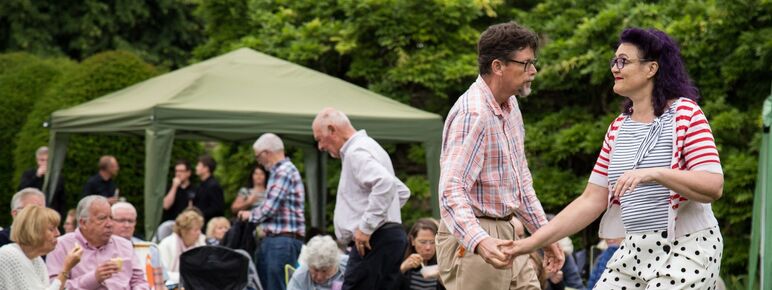 A photograph of a man and a women outside dancing on grass with an audience watching them
