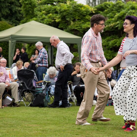 A photograph of a man and a women outside dancing on grass with an audience watching them