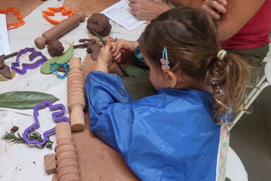 A photograph of a little girl in a blue apron carving into clay during a workshop at Watts Gallery