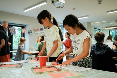 Two girls rolling out pink paint with rollers in a printmaking workshop