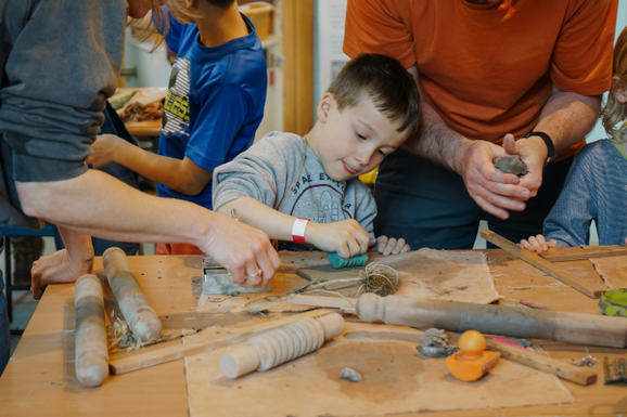 A young boy making with clay, surrounded by parents and other children taking part in the workshop.