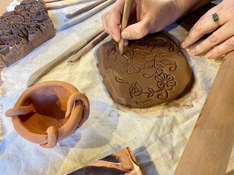 A close up photo of a woman's hand making marks on clay