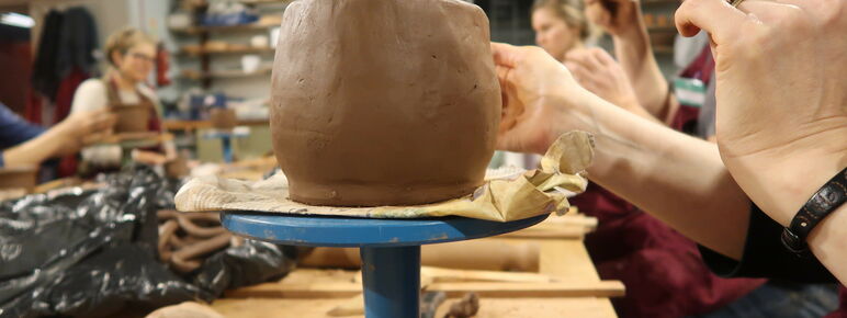 A close up of a clay pot on a blue stand at a pottery workshop