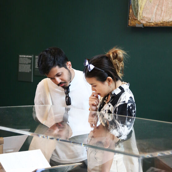 Two young people lean over a glass display case in the Mary Watts Gallery