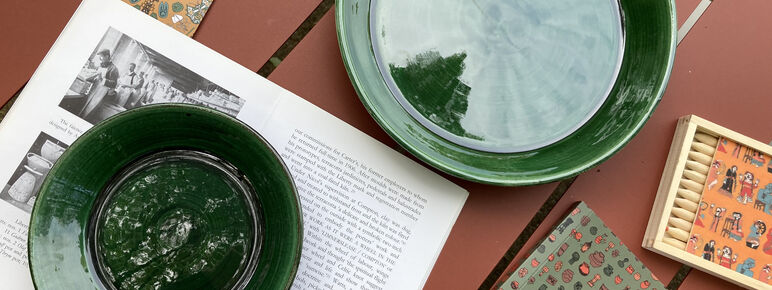 A green plate and bowl, a notebook and a set of colouring pencils are arranged across a terracotta background