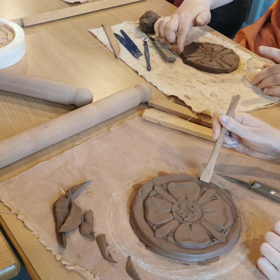 Two people shape clay coasters using palette knifes