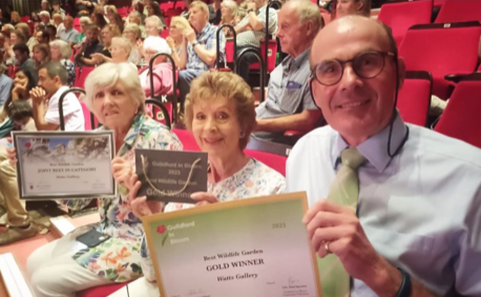 Two women and a man sitting in theatre seats, holding up a certificate for best wildlife garden.