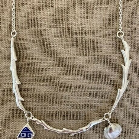 Photo of a silver necklace that looks like a flower stem, with a seashell and gem charm
