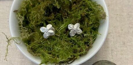 Photo of a bowl with moss in, with a pair of silver stud earrings and a ring placed in the moss which resemble flowers