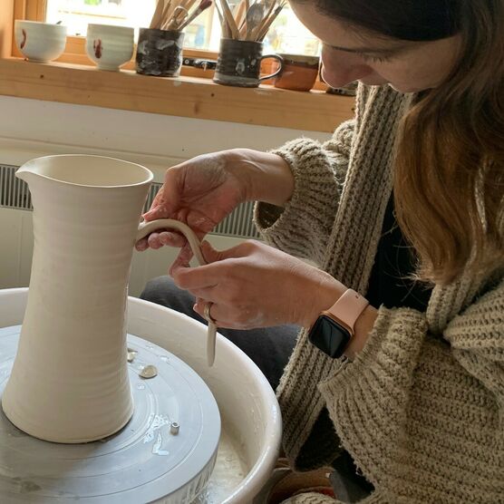 Photo of a woman with short brown hair making a jug from clay
