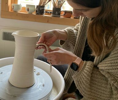 Photo of a woman with short brown hair making a jug from clay