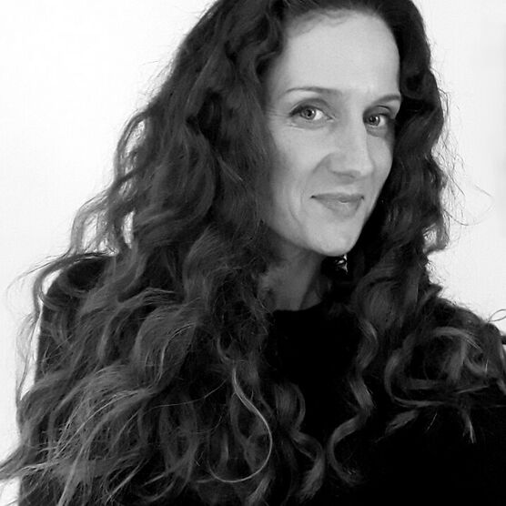 Black and white photo of a woman with long dark curly hair, smiling at the camera