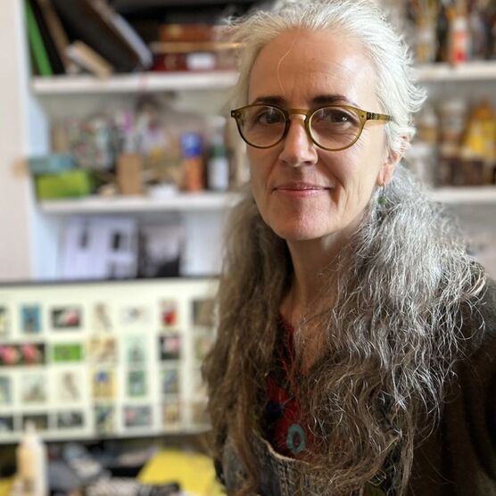 Photo of a woman with long grey curly hair and round glasses. She is facing the camera and smiling