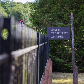 A simple slate sign with white writing says: Watts Cemetery Chapel