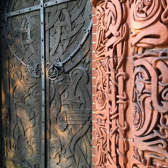Close up of the Chapel exterior door, the wooden door is covered with Celtic designs and so is the terracotta arch framing it