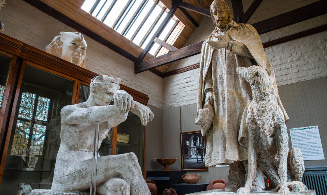 Plaster model of a women in foreground, with Alfred Lord Tennyson statue in background, featuring a man and dog