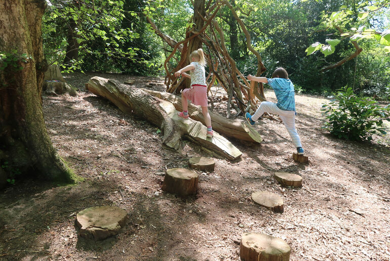 Two children jump from wooden stepping stones in woodland