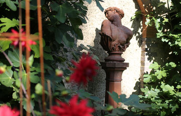 Terracotta bust of a women turning her head, outside surrounded by bright pink flowers