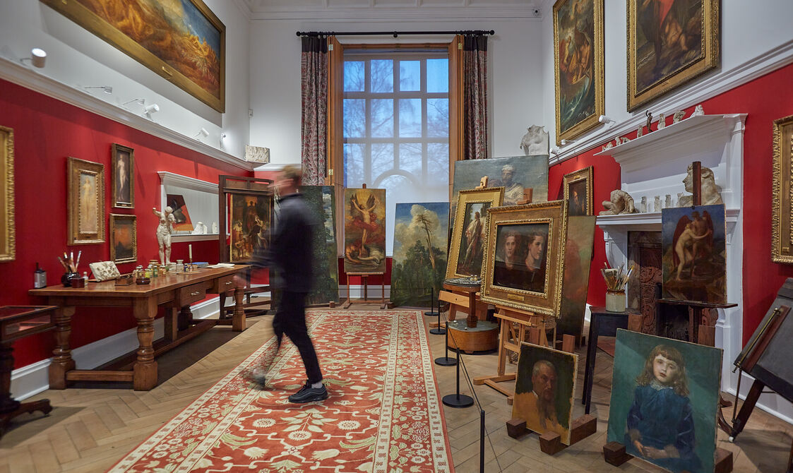 A red room with many paintings on wooden easels, a visitor walks past