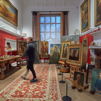 A red room with many paintings on wooden easels, a visitor walks past