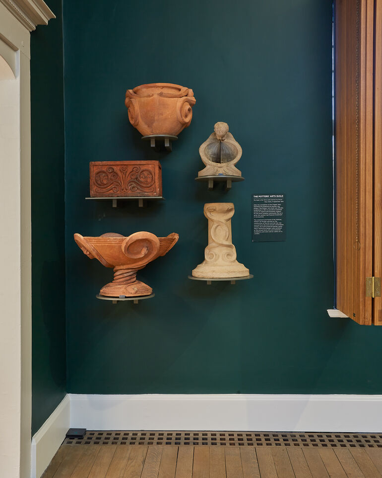 A green wall with five terracotta pottery pieces mounted