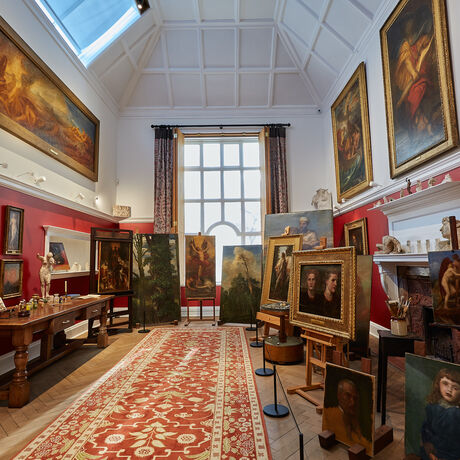 A red and white room filled with paintings on the wall and on easels