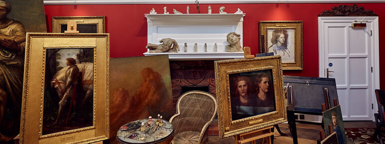 A white and red walled studio space with paintings on the wall and on easels