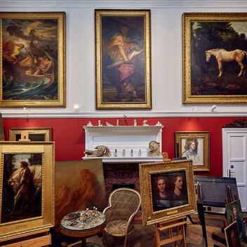 A white and red walled studio space with paintings on the wall and on easels