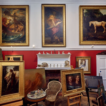 A white and red walled studio space with paintings on the wall and on easels