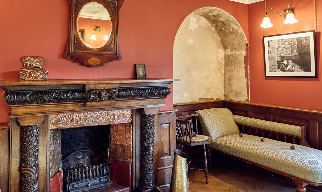 A red room featuring a wooden fireplace, mirror and chaise longue