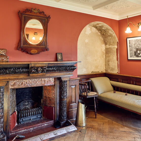 A red room featuring a wooden fireplace, mirror and chaise longue