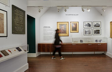 White gallery space featuring portraits and photos, a visitor walks past