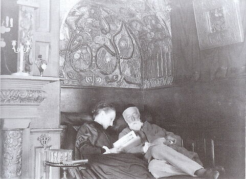Archive black and white photo of George and Mary, Mary reads to George underneath a decorated arch way