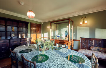 A green room with a dining table, chairs and period furniture