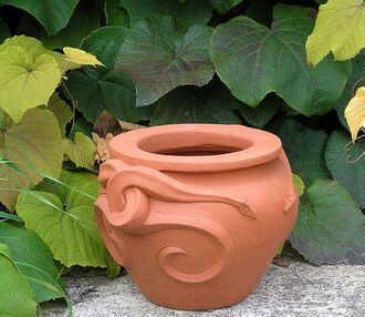 A photo of a terracotta snake pot against a backdrop of green ivy