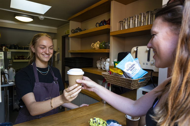 A staff member in the Watts Tea Shop hands a hot drink to a customer whilst smiling
