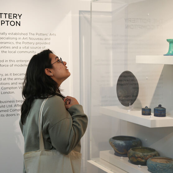 A young woman looks at examples of Compton pottery in a glass display case